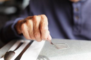 A senior man holding his fork while waiting for his meal to arrive at a restaurant. Intentional extremely shallow depth of field.